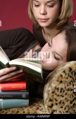 Deux jeunes filles, pré-adolescents, adolescentes portant sur un tigre-print canapé avec une pile de livres scolaires Banque D'Images