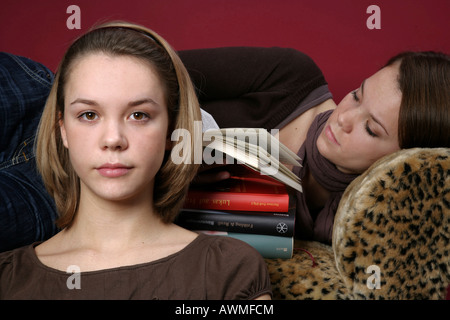 Deux jeunes filles, pré-adolescents, début de l'adolescence sur un canapé pour lire un livre ensemble Banque D'Images