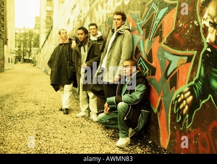 Cinq jeunes hommes appuyé contre mur recouvert de graffitis, pleine longueur Banque D'Images