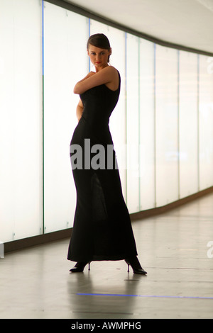 Jeune femme portant robe de soirée noir debout devant un mur de cibles dans un passage pour piétons Banque D'Images