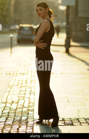 Jeune femme portant robe de soirée noir debout sur une rue pavée Banque D'Images