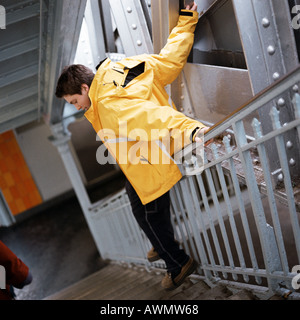 Teenage boy dans l'imperméable en glissant sur la rampe d'escalier en Banque D'Images