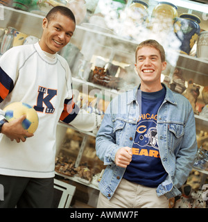 Les jeunes hommes appuyé contre la fenêtre de magasin, smiling, face caméra. Banque D'Images