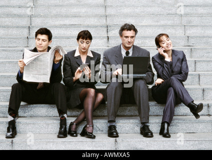 Quatre personnes portant des costumes, sitting on steps Banque D'Images