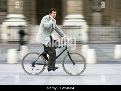 Homme portant costume, cell phone et riding bike, floue. Banque D'Images