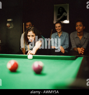 Jeune femme jouer au billard, les jeunes gens assis en arrière-plan Banque D'Images