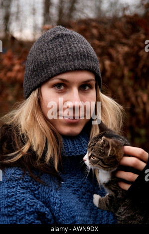 Portrait d'une jeune femme blonde wearing wool hat, tenant un petit chat sur son bras Banque D'Images