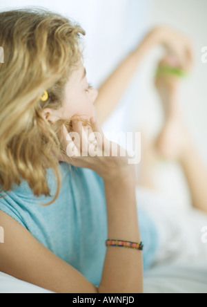 Preteen girl lying on stomach, remontant pour pied Banque D'Images