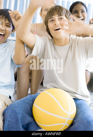 Groupe d'élèves du secondaire assis avec le basket-ball, cheering Banque D'Images