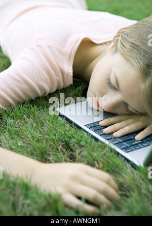 Adolescente dans l'herbe, allongé avec la tête sur un ordinateur portable Banque D'Images