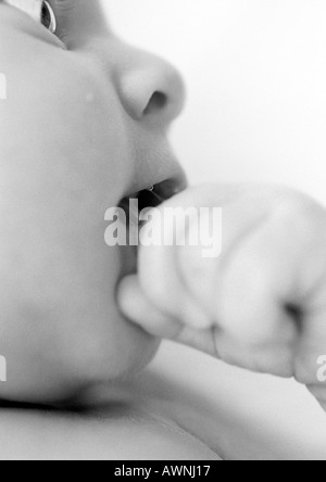 Vue partielle de visage du bébé avec la main à la bouche, B&W. Banque D'Images