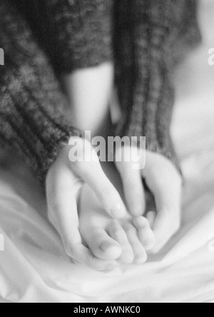 Femme assise, close-up of hands holding pied, B&W. Banque D'Images