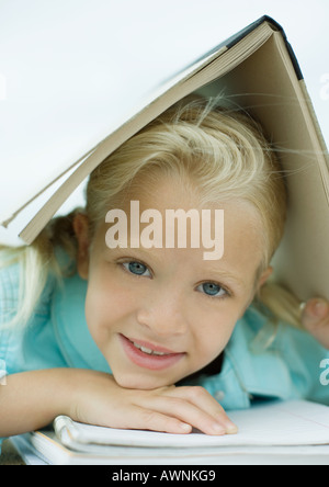 Girl holding book over head, smiling Banque D'Images