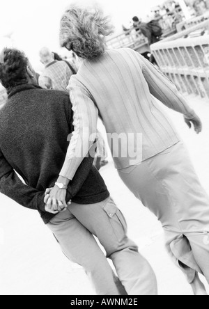 Mature couple walking down boardwalk tenant les mains, vue arrière, B&W Banque D'Images