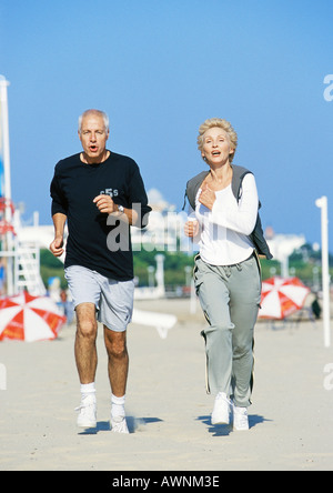 Mature couple jogging on beach, vue avant, pleine longueur Banque D'Images