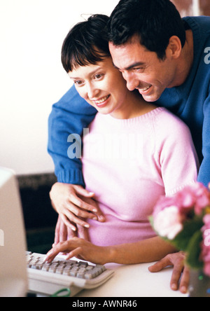 Femme enceinte à l'aide d'ordinateur, l'homme avec les bras autour d'elle à par-dessus son épaule Banque D'Images