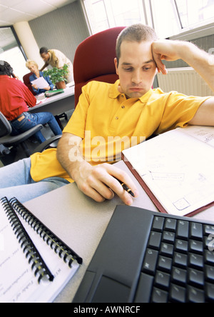 Young man sitting in office, vous courber en président, les gens qui travaillent en arrière-plan Banque D'Images