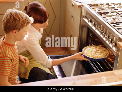 Woman putting tarte dans un four, l'observation de l'enfant Banque D'Images