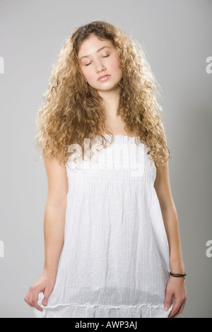 Jeune femme avec de longs cheveux bouclés, vêtue d'une robe blanche Banque D'Images