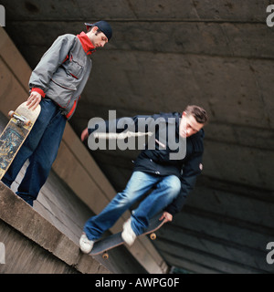 Deux adolescents avec des planches à roulettes, un saut vers le bas d'un mur Banque D'Images