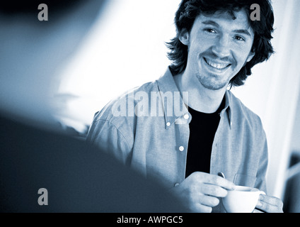Man holding teacup, souriant, à la deuxième personne en premier plan, floue Banque D'Images