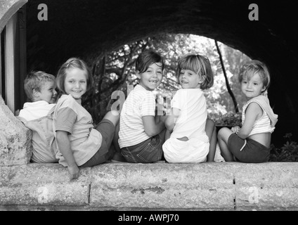 Cinq enfants assis sous une arche, b&w Banque D'Images