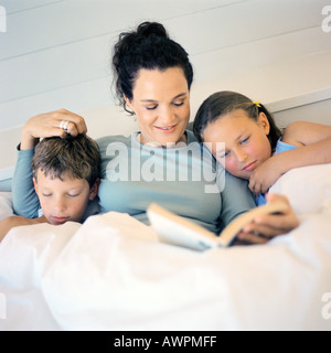 Mère au lit entre les enfants, reading book Banque D'Images