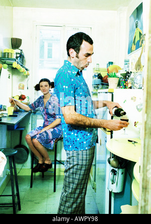 Couple in kitchen, femme assise, l'homme de verser le vin. Banque D'Images