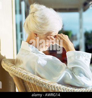 Senior woman sitting in sun avec la main au-dessus des yeux, side view Banque D'Images