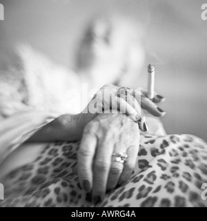 Young woman's hands holding cigarette, low angle view, b&w Banque D'Images