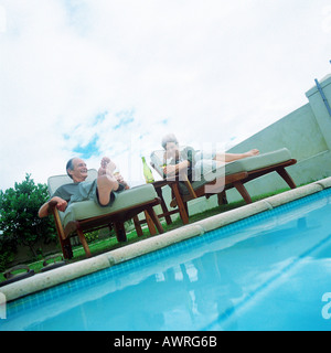 Mature couple lying in lounge chaises à côté piscine Banque D'Images