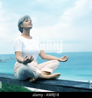 Mature Woman sitting on wooden rail en position du lotus, portrait Banque D'Images