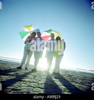 Deux couples matures standing on beach, des parasols Banque D'Images