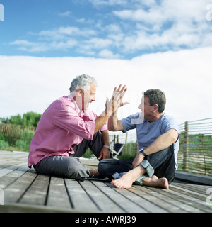 Les hommes d'âge mûr assis ensemble, slapping mains dans l'air, sur le pont à l'extérieur Banque D'Images