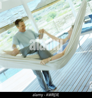 Young woman laughing in hammock, mature man empoignant ses bras et jambes, blurred Banque D'Images