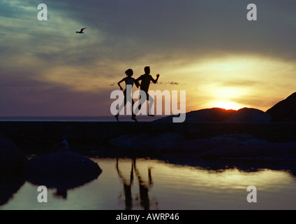 Couple running près de l'eau au coucher du soleil, silhouette Banque D'Images