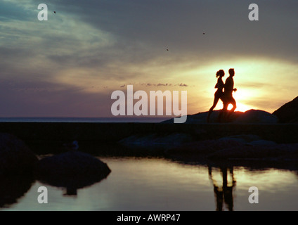 Couple running près de l'eau au coucher du soleil, silhouette Banque D'Images