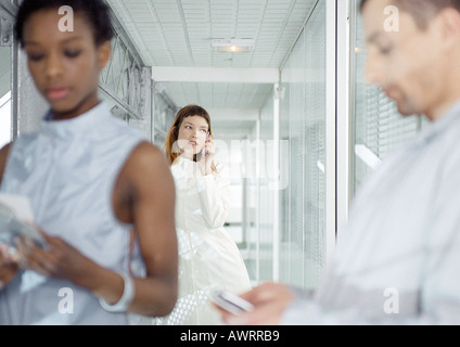 Trois personnes dans le couloir, l'un using cell phone Banque D'Images