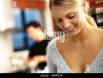 Dans la cuisine, woman smiling and looking down, man in background Banque D'Images