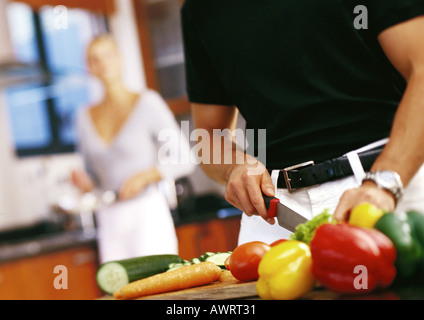 Man cutting vegetables, mi-section, femme debout en arrière-plan Banque D'Images