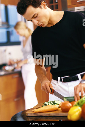 Man slicing vegetables in kitchen, mi-section Banque D'Images