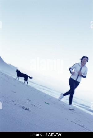 Young woman running on beach, le chien en arrière-plan Banque D'Images