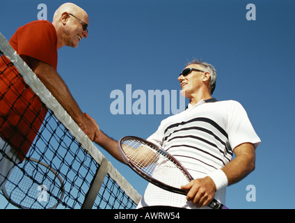 Deux hommes matures se serrer la main au filet de tennis, low angle view Banque D'Images