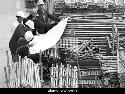 Cinq personnes examining blueprints in construction site, b&w Banque D'Images