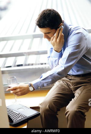 Man with cell phone, tenant un verre de vin et de pointing at laptop Banque D'Images