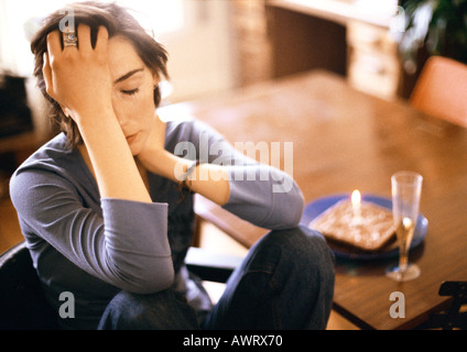 Woman at table, holding head Banque D'Images