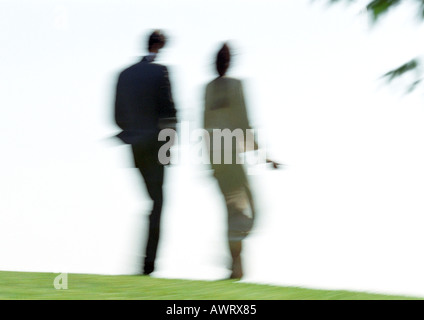 Businessman and woman walking on grass, vue arrière, blurred Banque D'Images