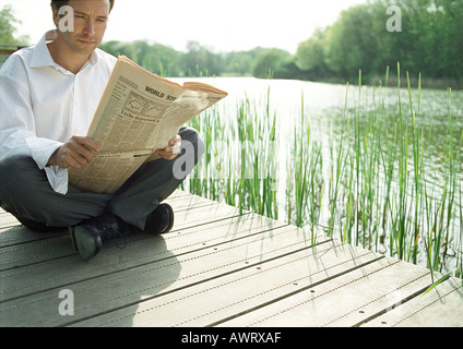 Homme assis à l'extérieur, reading newspaper Banque D'Images