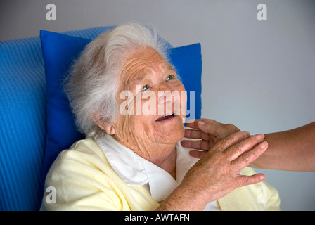 Sourire de contentement femme âgée regarde et touche main réconfortante de soignant Banque D'Images