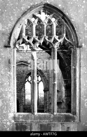 Voir à travers un glassless fenêtre cintrée d'une église à l'abandon par des pyromanes brûlé et laissé comme une ruine en monochrome Banque D'Images